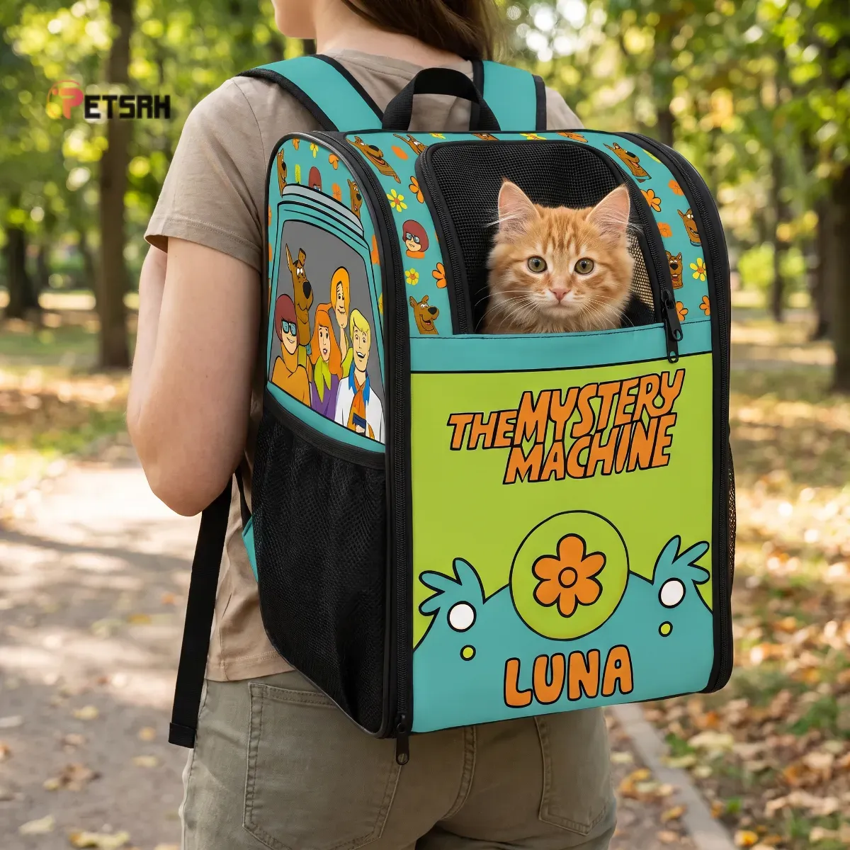Personalized Mystery Machine pet backpack worn in a sunlit park with a ginger cat inside.