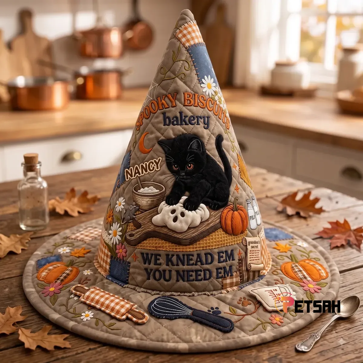 Front view of a brown quilted fabric witch hat with a detailed Spooky Biscuits Bakery design featuring a black cat and autumn imagery.